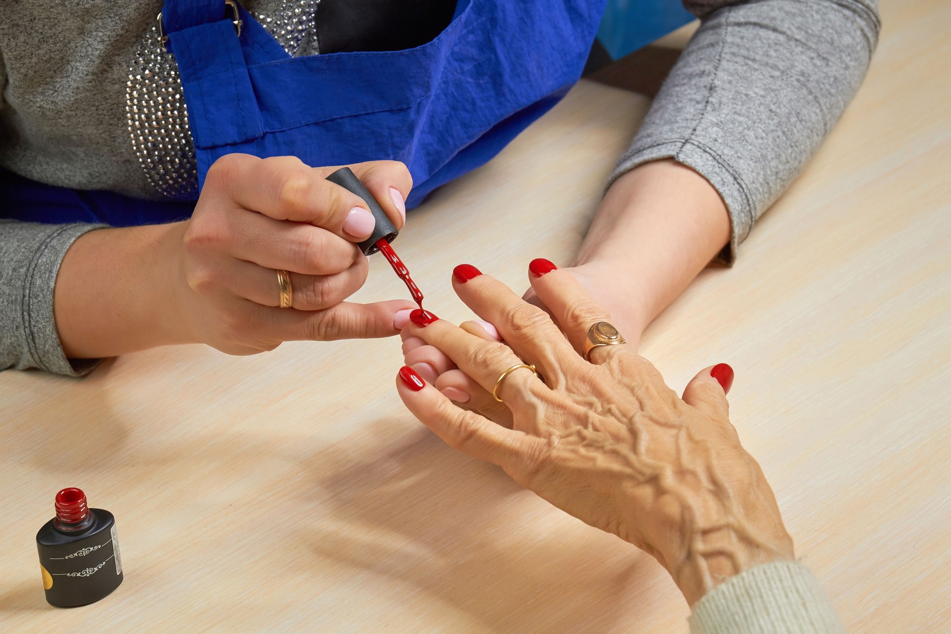 Beautician applying red varnish to woman nails.